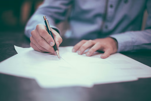 A close-up of someone signing paperwork on a desk.